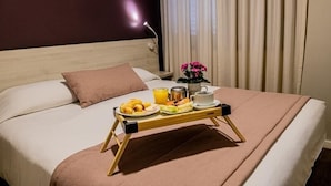 A neatly made bed with a tray of breakfast items including croissants, fruit, and beverages, a bedside lamp, and a vase with flowers. - Travel Inn Flats Jardins (São Paulo)