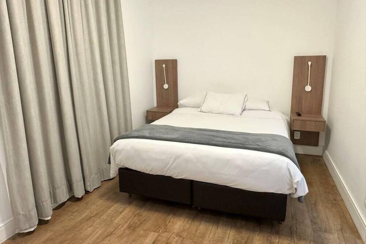 A bedroom with a bed, curtains, wooden nightstands, and a wooden floor.