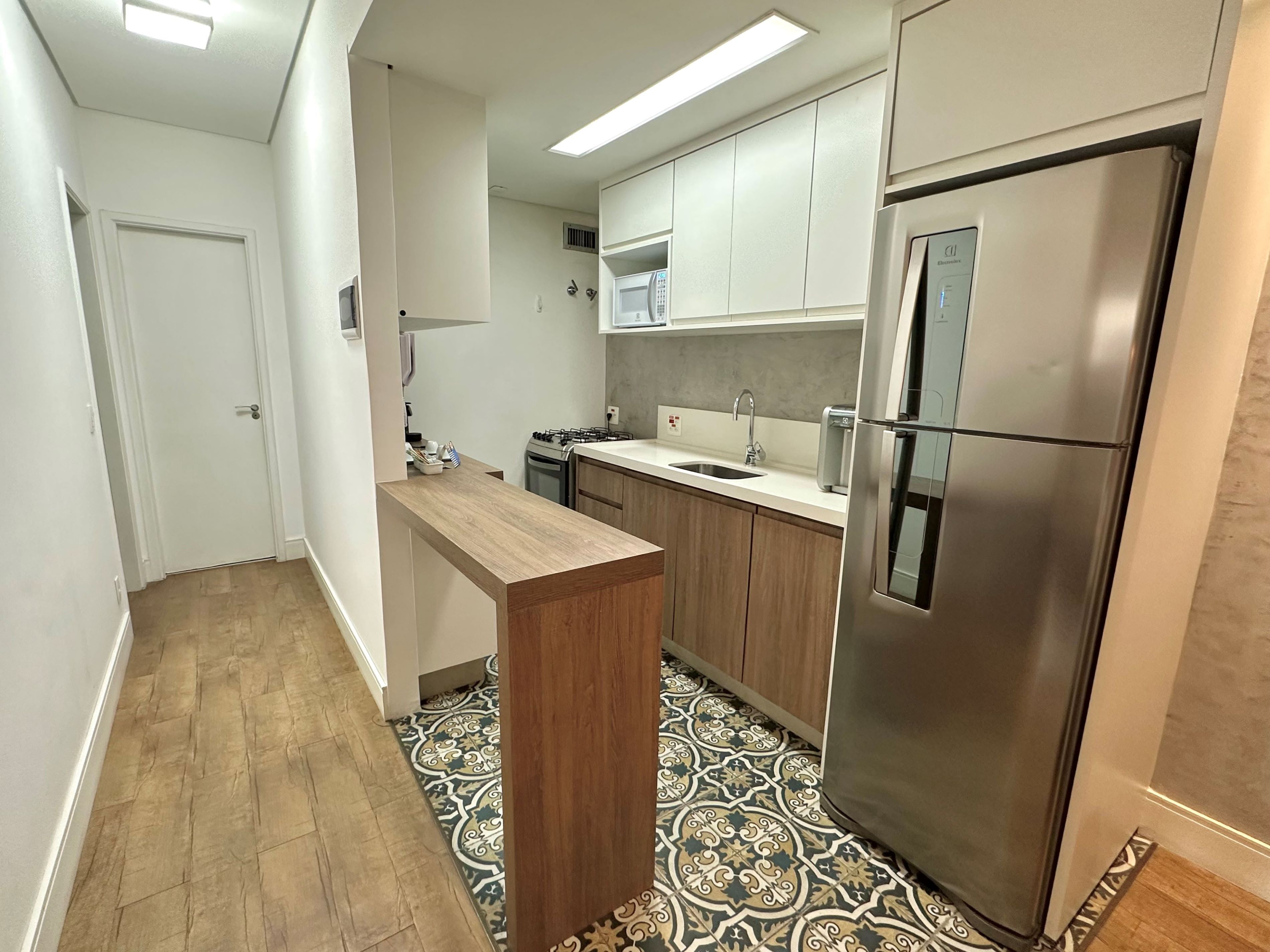 Une cuisine moderne avec des meubles en bois, un réfrigérateur en acier inoxydable et un sol carrelé à motifs.