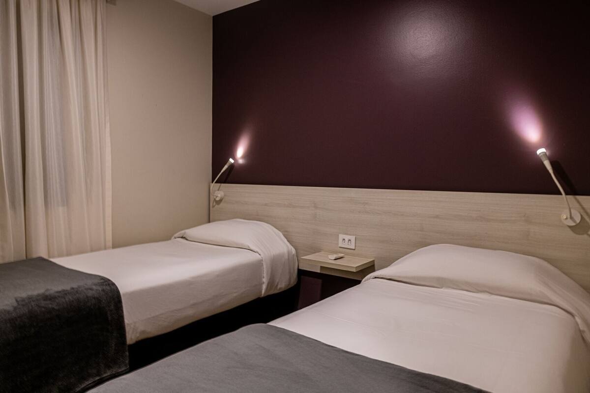 A hotel room with two single beds, a nightstand, a lamp, and a power outlet.