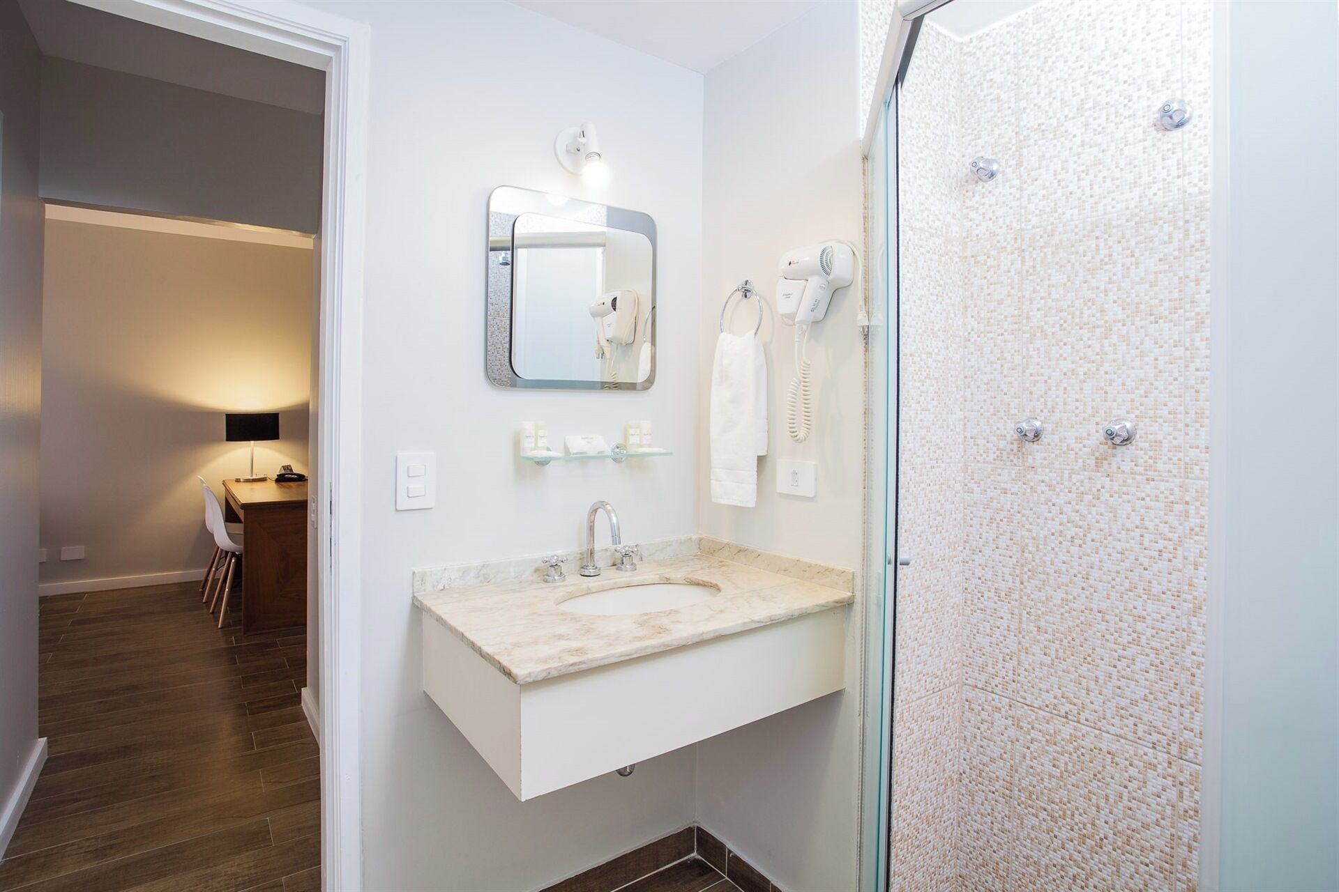A modern bathroom with a marble sink, a large mirror, a hairdryer, and a towel rack.