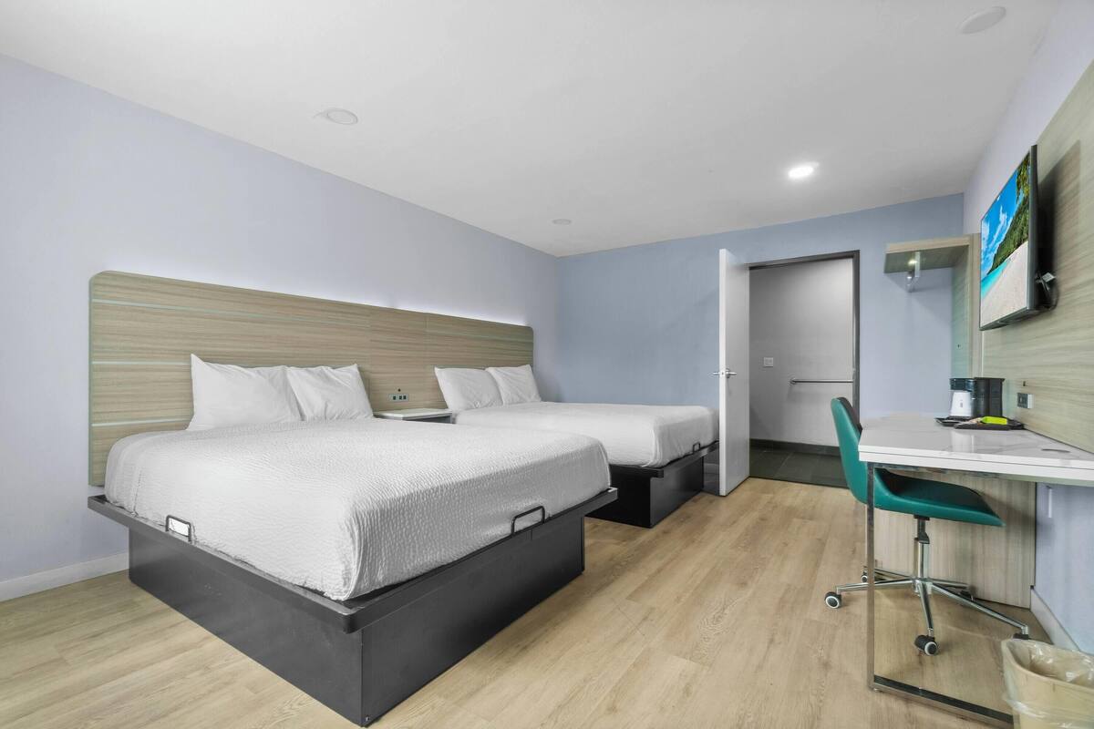 A modern hotel room with two beds, a desk, and a chair.