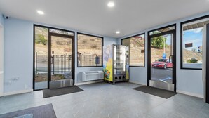 Un interior moderno con ventanas amplias, una máquina expendedora y un estacionamiento visibles a través de las puertas de vidrio.