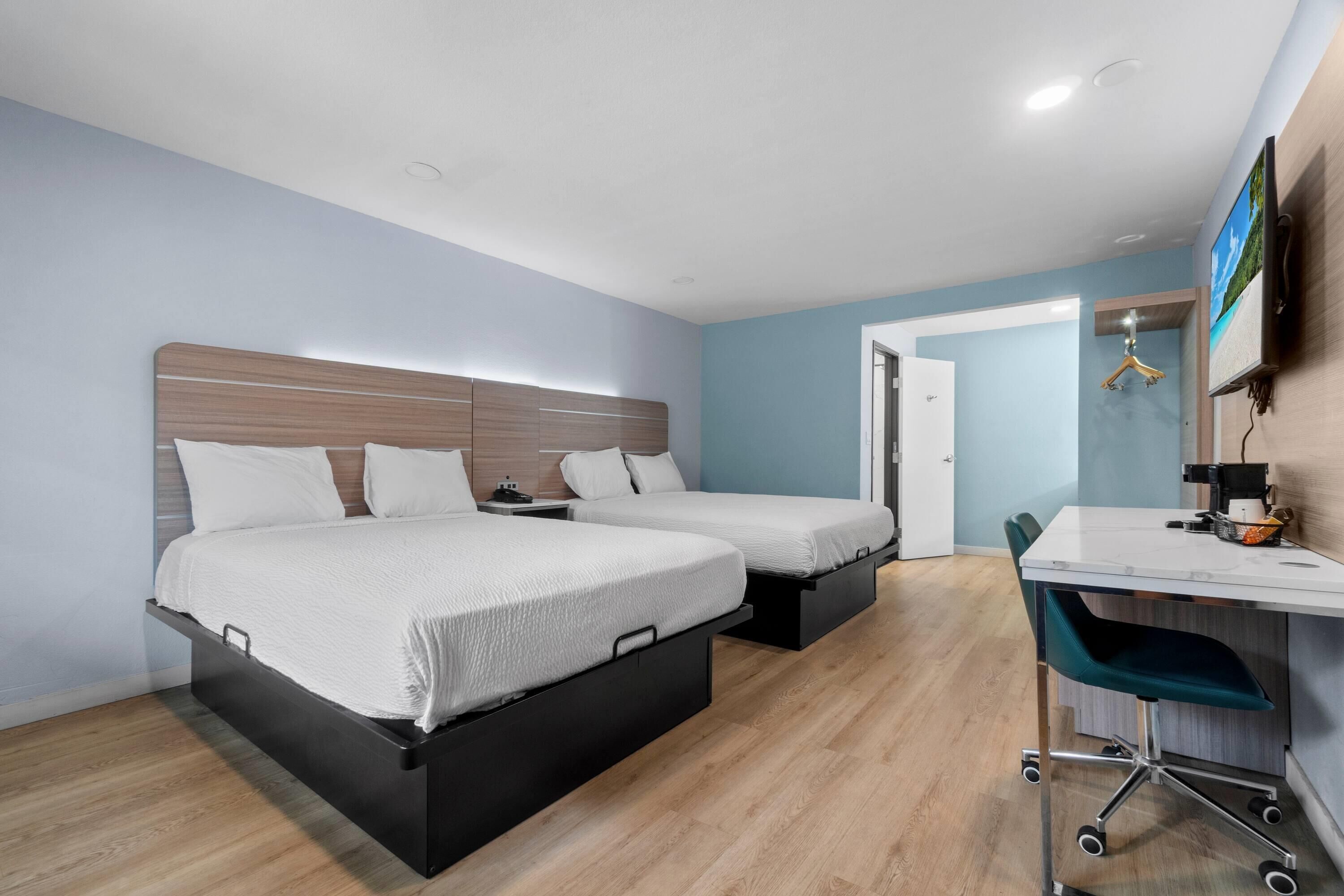 Una habitación de hotel con dos camas, un escritorio con silla, un televisor y un armario.
