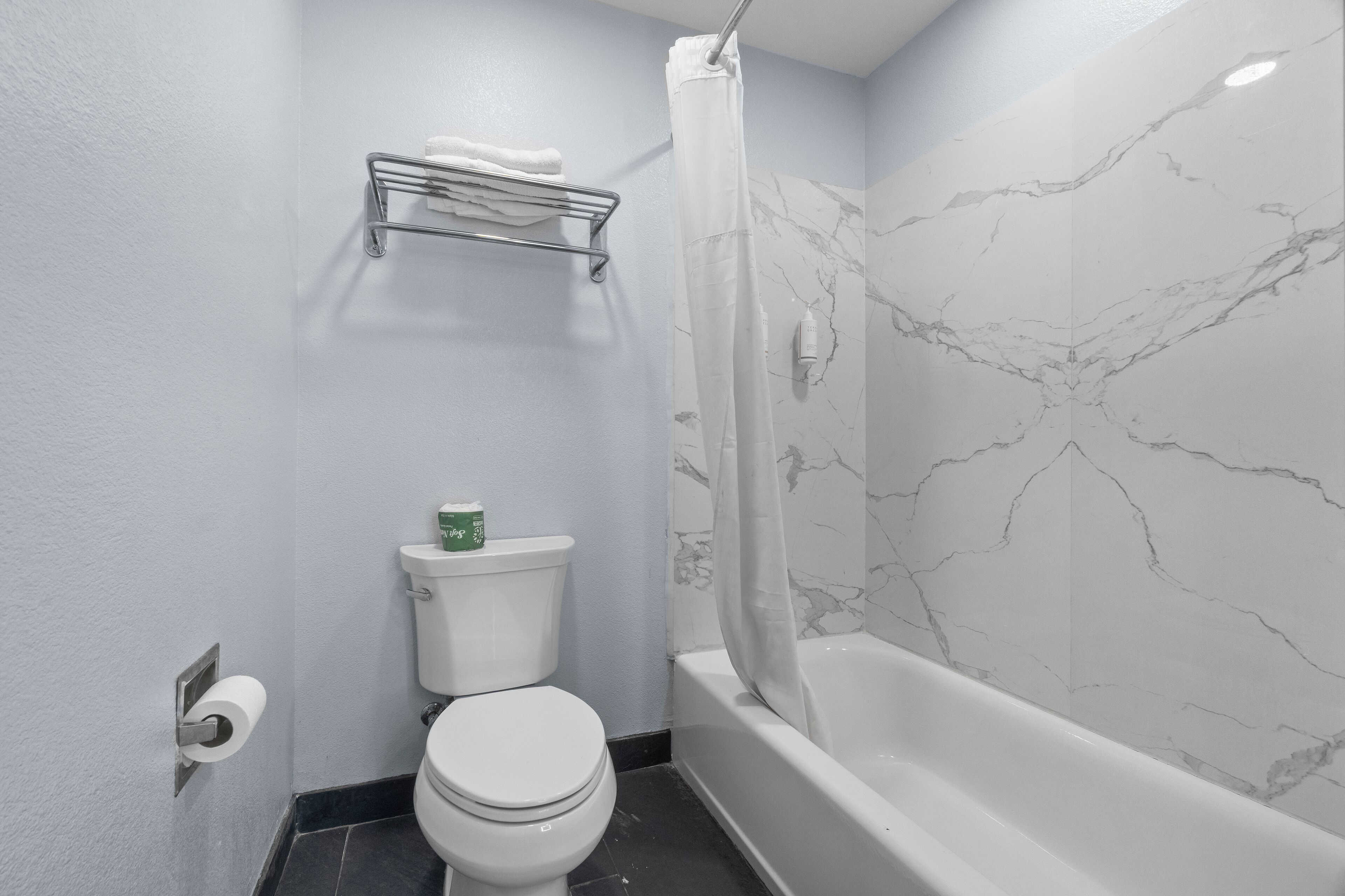 Un baño con inodoro, toallero, cortina de ducha y bañera.