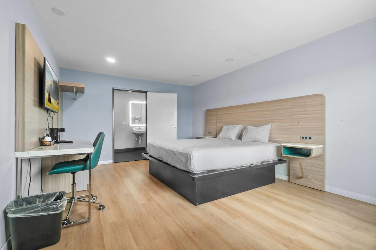 A modern bedroom with a bed, desk, chair, and a small trash bin.