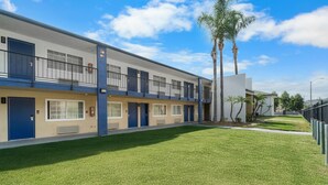 Un motel moderno con una estructura de dos pisos, varias habitaciones con puertas azules y un césped bien cuidado.