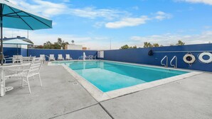 Una piscina con sillones de descanso y sombrillas, rodeada por un muro azul y un cielo despejado.