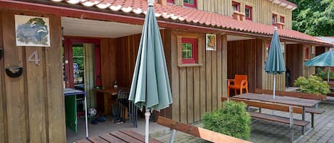 A wooden building with a red-tiled roof, outdoor seating with benches and umbrellas, and a small table with chairs.