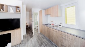 A modern kitchen with wooden cabinets, a built-in TV, and a window with blinds.