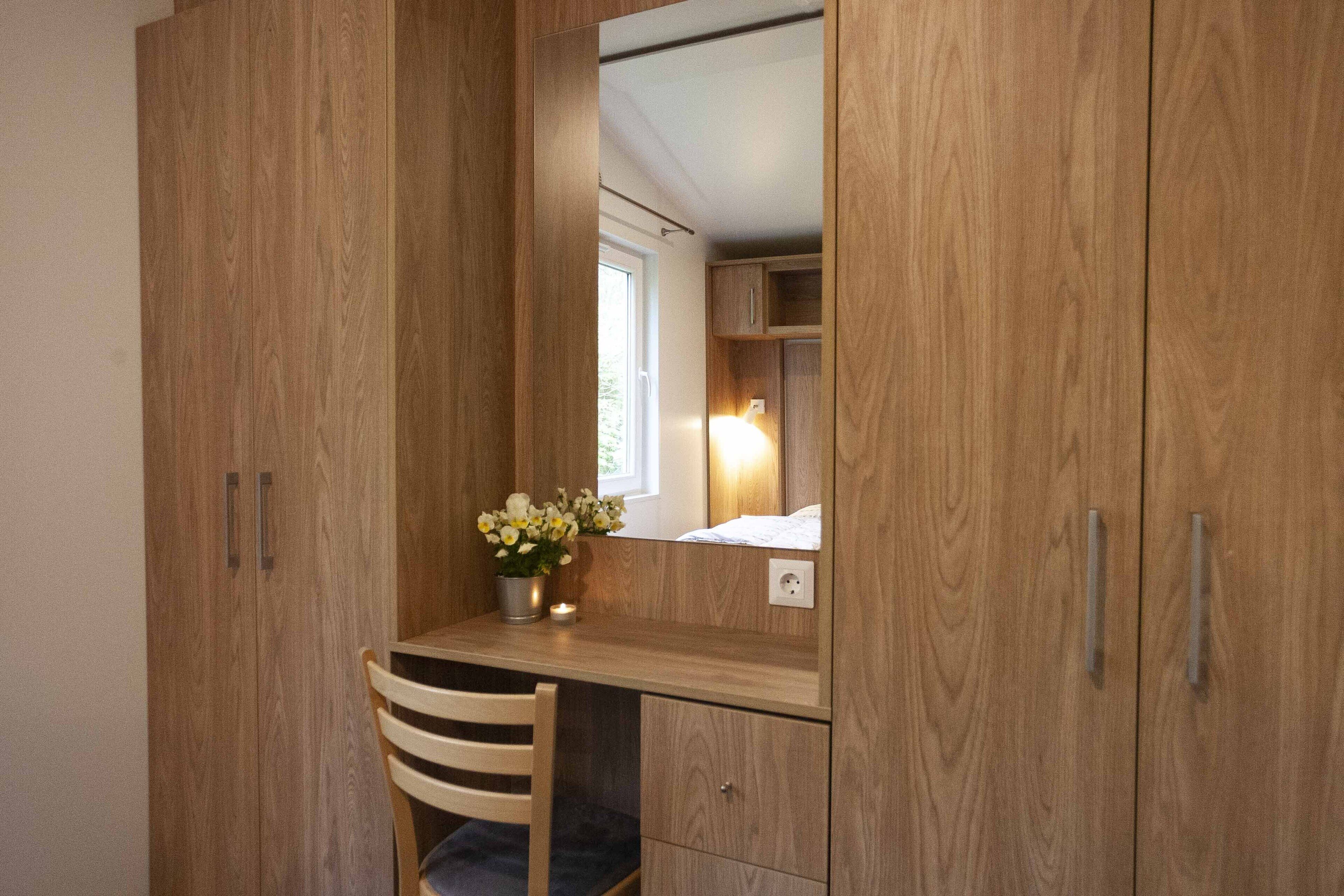 A wooden wardrobe with a mirror, a desk, and a chair.
