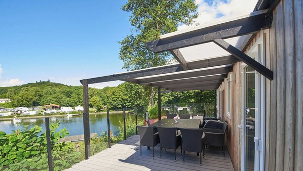 A deck with a table and chairs overlooking a body of water, with a covered area and a building adjacent to it.