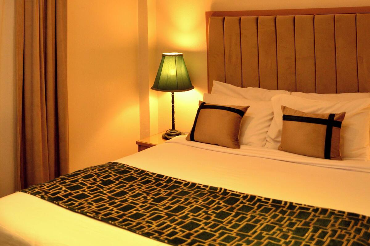 A hotel room with a bed, a nightstand, a lamp, and a window with curtains.