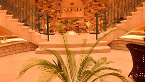A grand hotel lobby with a central staircase, a stone wall with a sign, and a palm plant in the foreground. - Dive Inn Resort (Sharm El Sheikh)