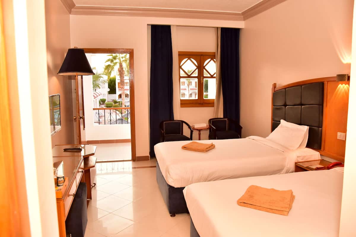 A hotel room with two beds, a desk, a chair, a small table, and a window with curtains.