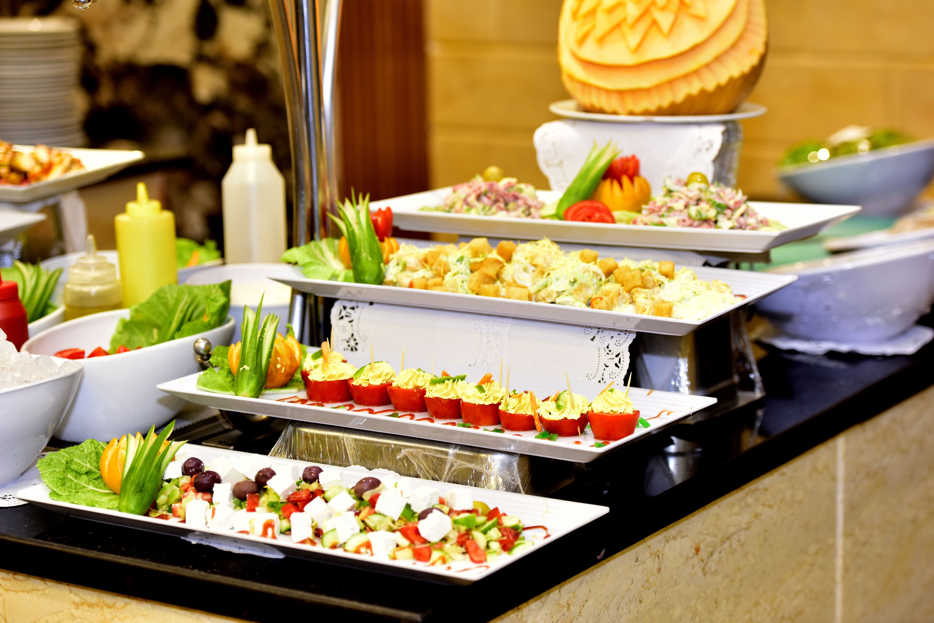 A buffet with various dishes including salads, appetizers, and a carved pumpkin centerpiece.