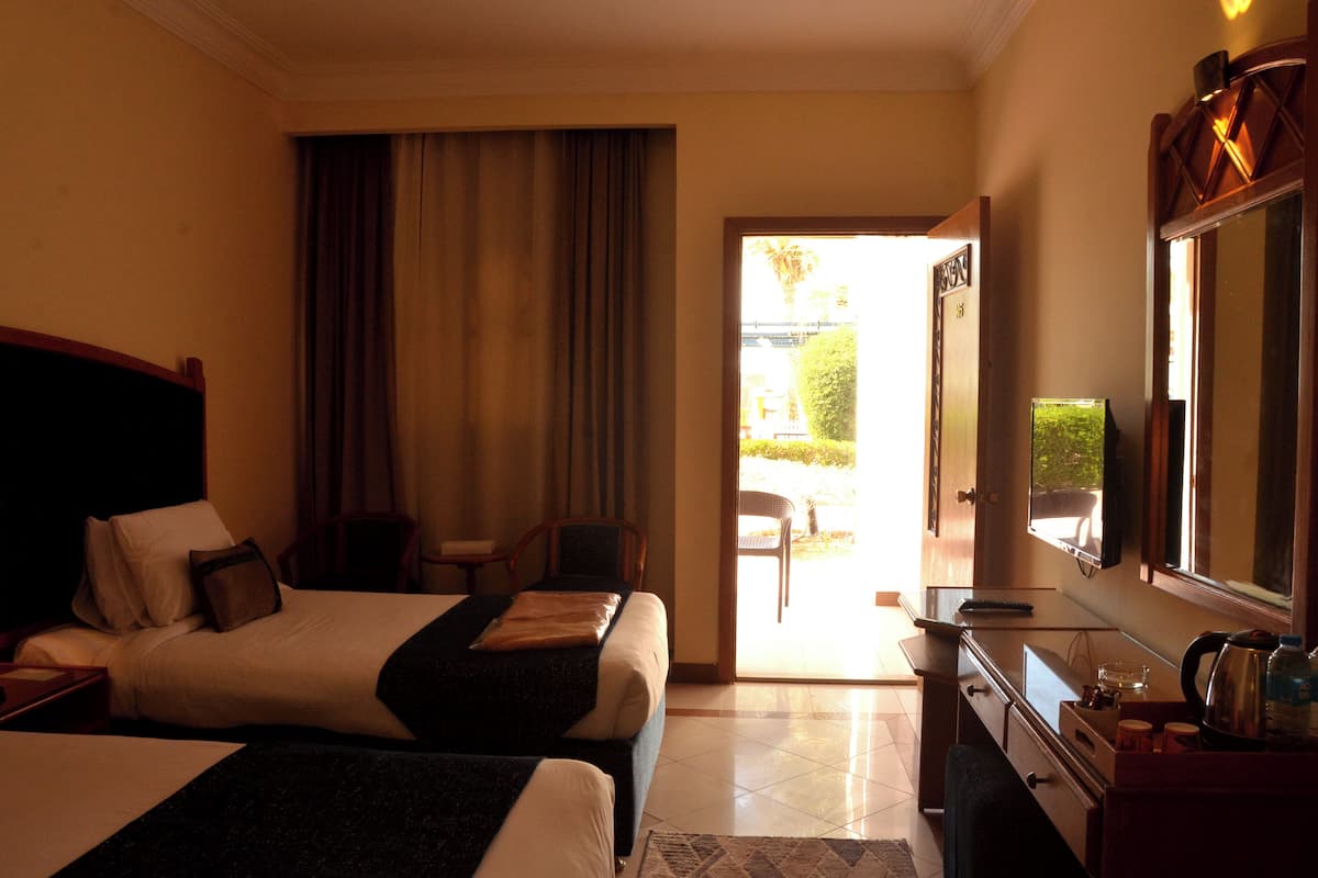 A hotel room with two beds, a desk, a chair, a television, and a view of the outdoors.