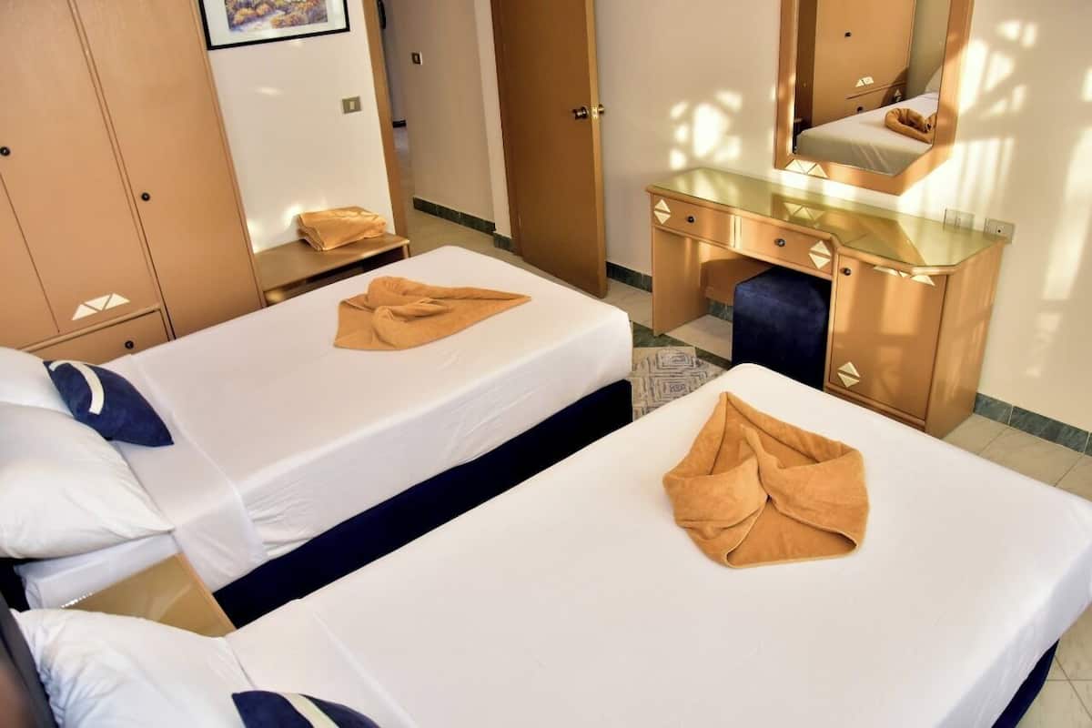 A hotel room with two beds, a desk, a mirror, and a wardrobe.