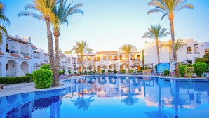 A swimming pool surrounded by palm trees and white buildings with balconies. - Dive Inn Resort (Sharm El Sheikh)