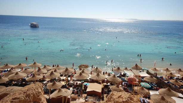 A beach with thatched umbrellas and sun loungers, a boat in the water, and people swimming. - Dive Inn Resort (Sharm El Sheikh)