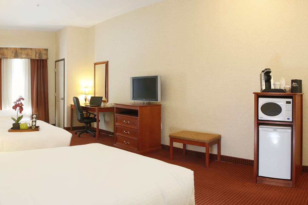 A hotel room with two beds, a desk with a computer, a television, a microwave, and a small refrigerator.