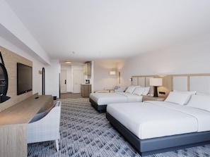 A hotel room with two beds, a desk, a flat-screen TV, a kitchenette, and a patterned carpet. - Pomeroy Inn & Suites Hotel Dawson Creek (Dawson Creek)