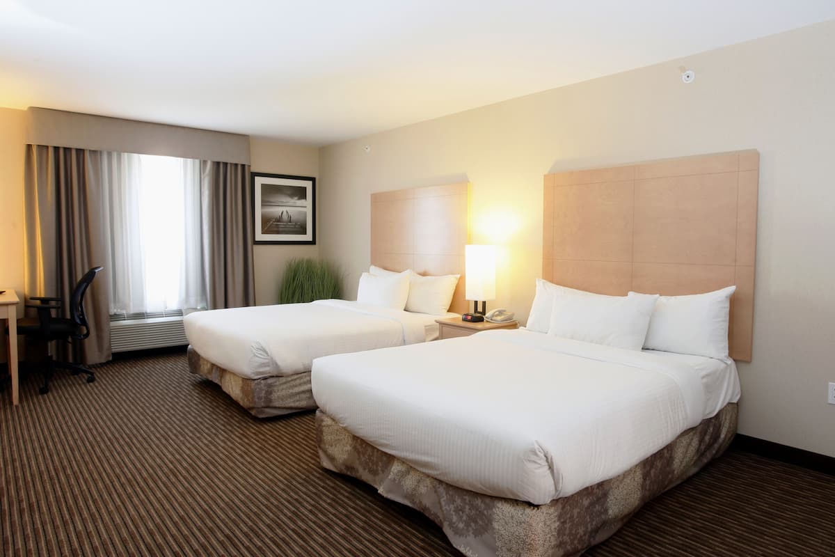 A hotel room with two beds, a desk, a chair, a lamp, and a window with curtains.