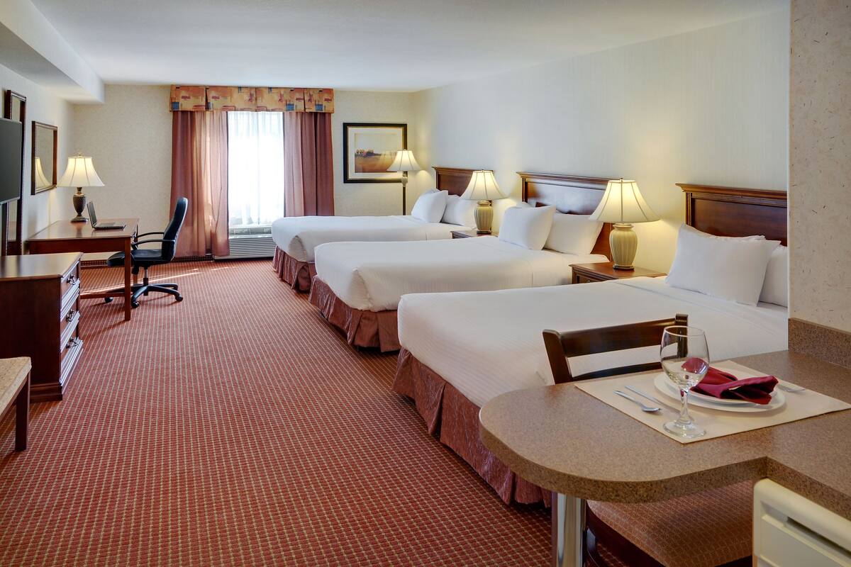 A hotel room with two beds, a desk, a chair, a TV, and a dining area with a table and chairs.