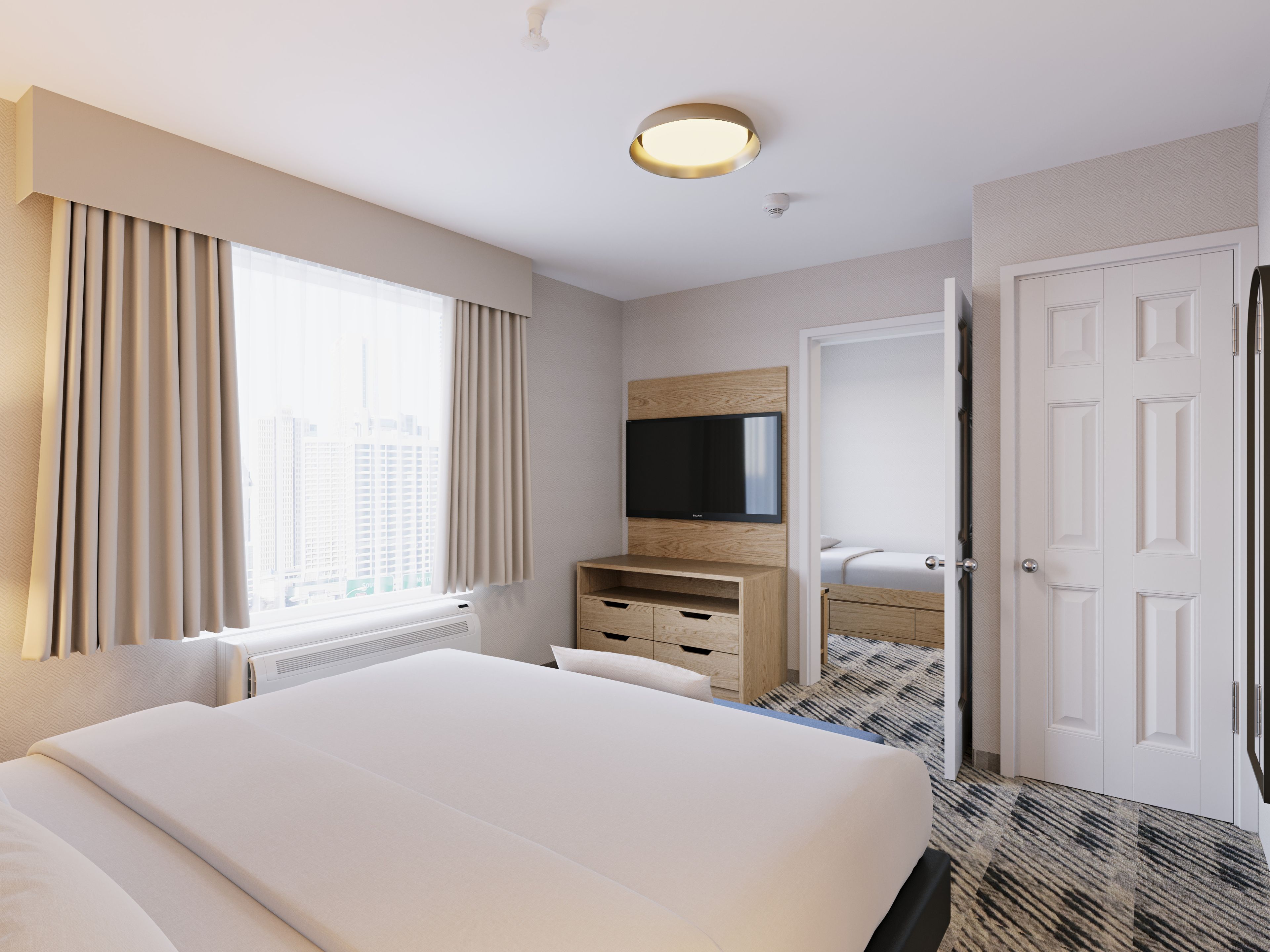 Quarto de hotel com uma cama grande, TV de tela plana, cômoda de madeira e porta que dá para outro quarto.