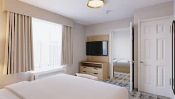 A hotel room with a large bed, a flat-screen TV, a wooden dresser, and a door leading to another room.