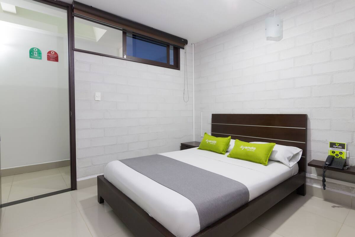 A hotel room with a bed, a nightstand, a window, and a wall-mounted phone.