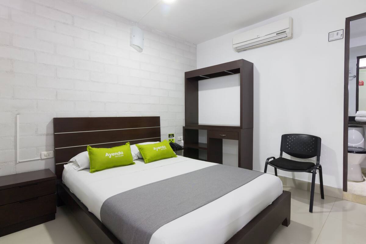 A hotel room with a bed, a nightstand, a chair, a desk, and a mirror.