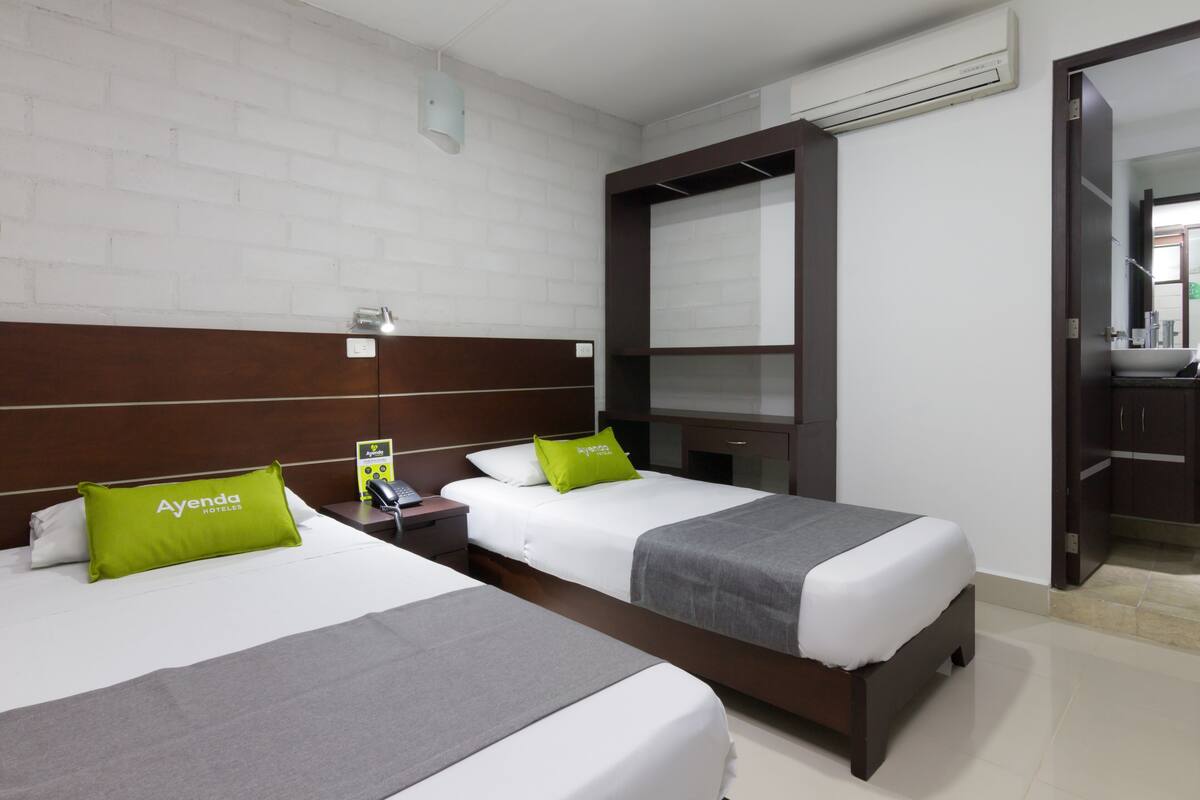 A hotel room with two beds, white walls, a wooden headboard, and a mirror.
