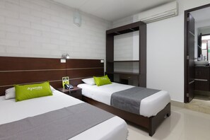 A hotel room with two beds, white walls, a wooden headboard, and a mirror.