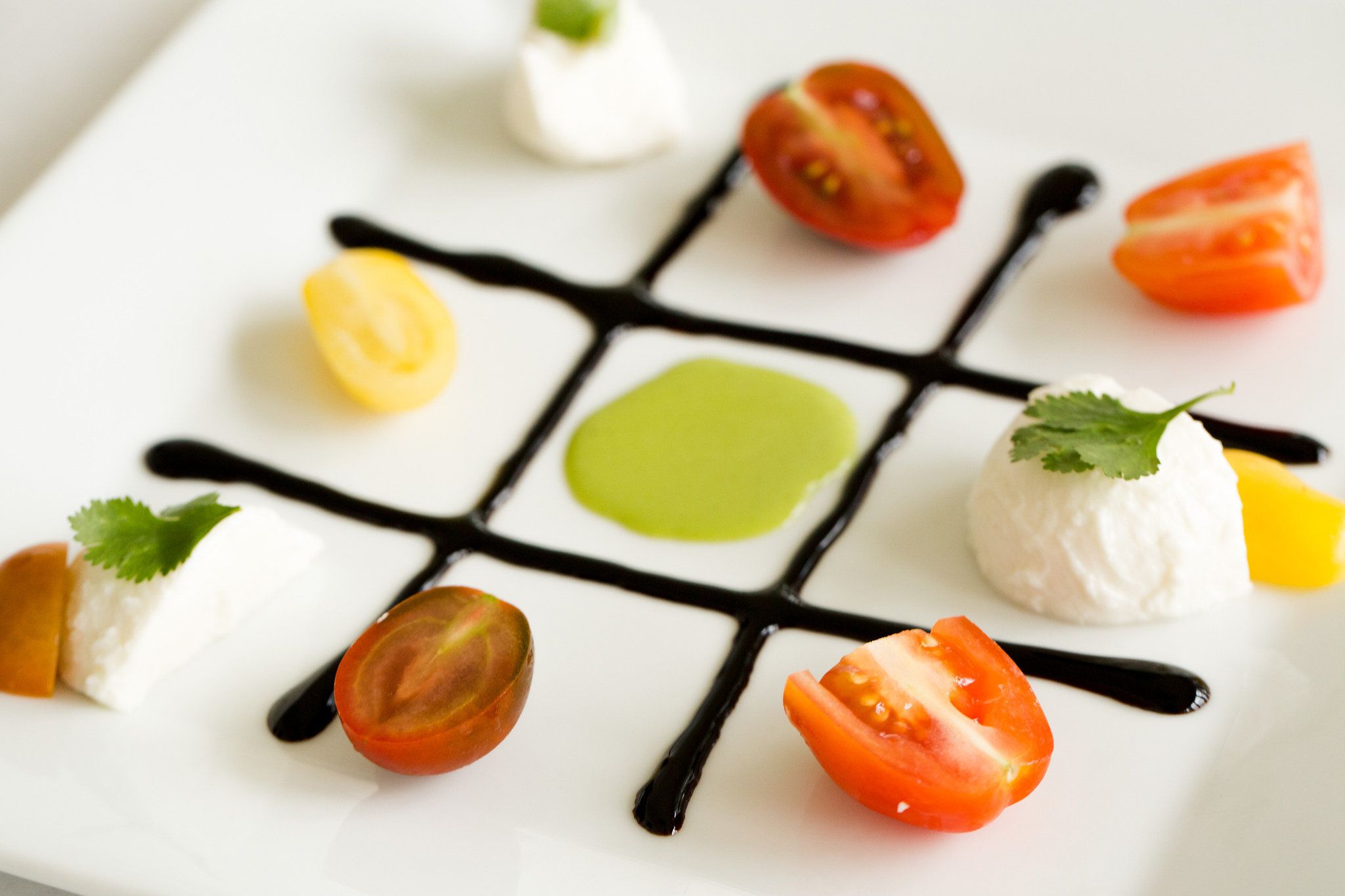 Une assiette blanche sur laquelle sont disposés divers aliments, notamment des tomates, une tranche jaune et une boule de fromage blanc, le tout agencé sur un motif quadrillé noir.