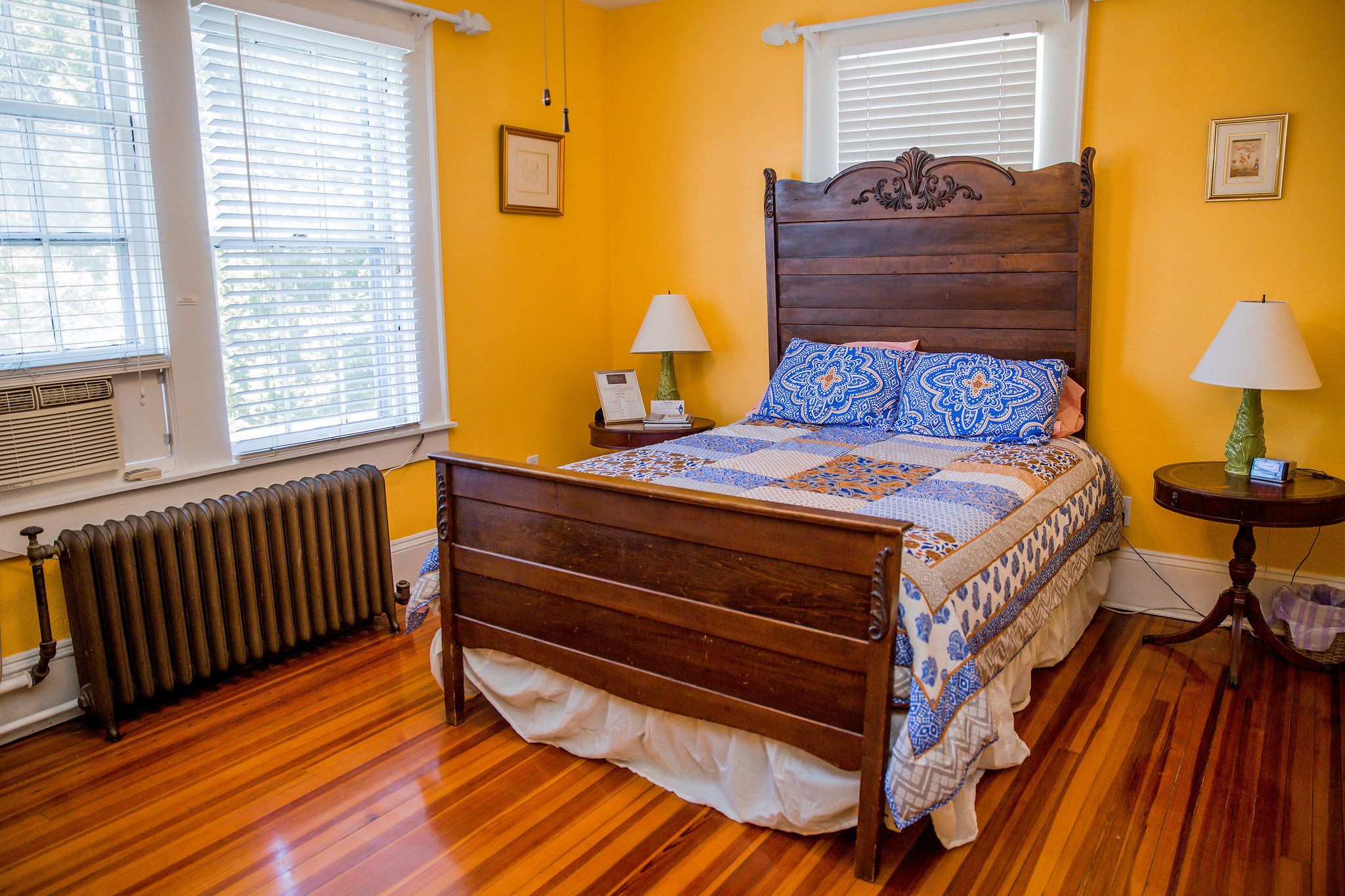 A bedroom with a wooden bed, two bedside tables, a radiator, and a window with blinds.