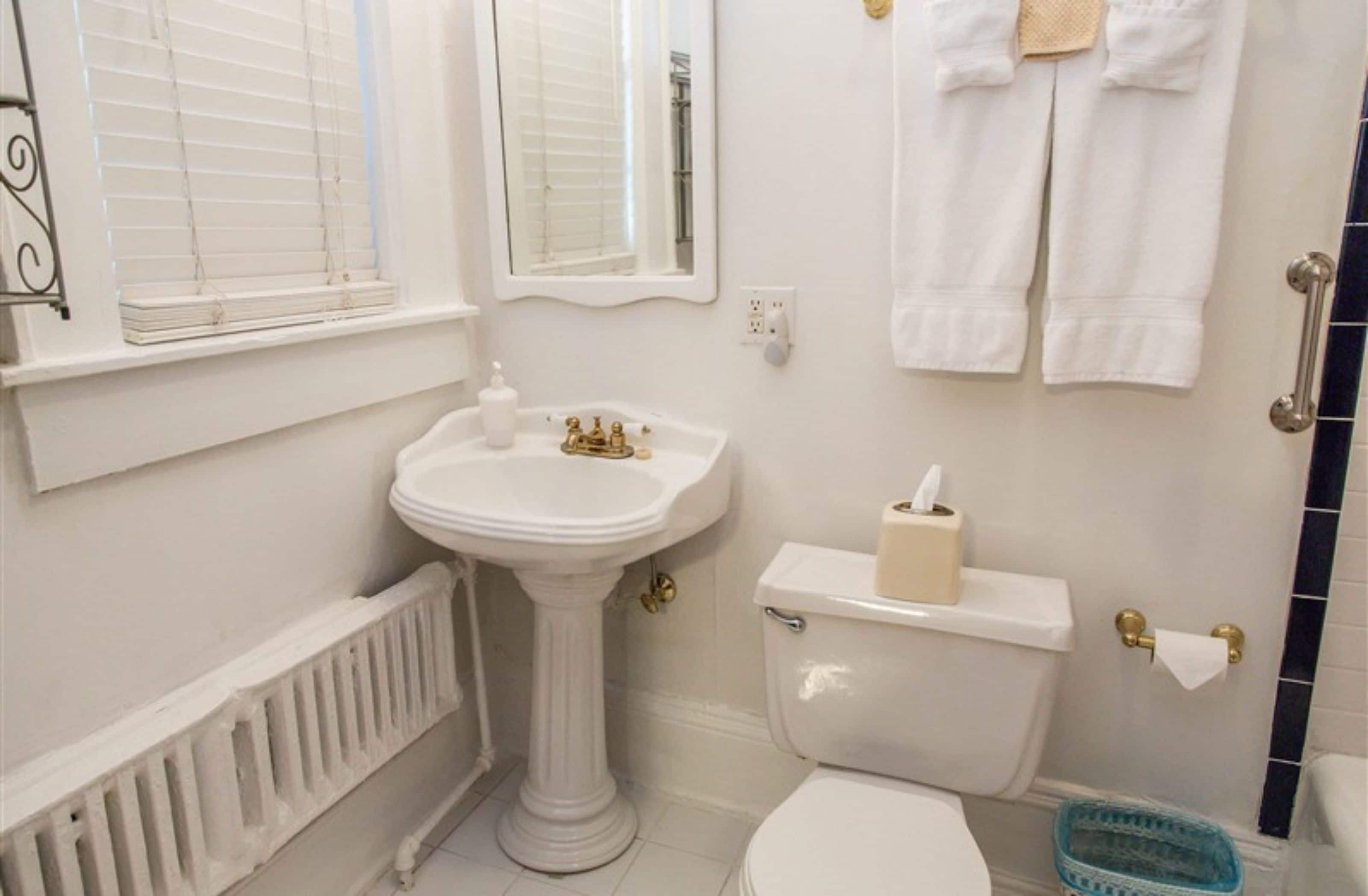 A bathroom with a pedestal sink, toilet, and a towel rack with towels.