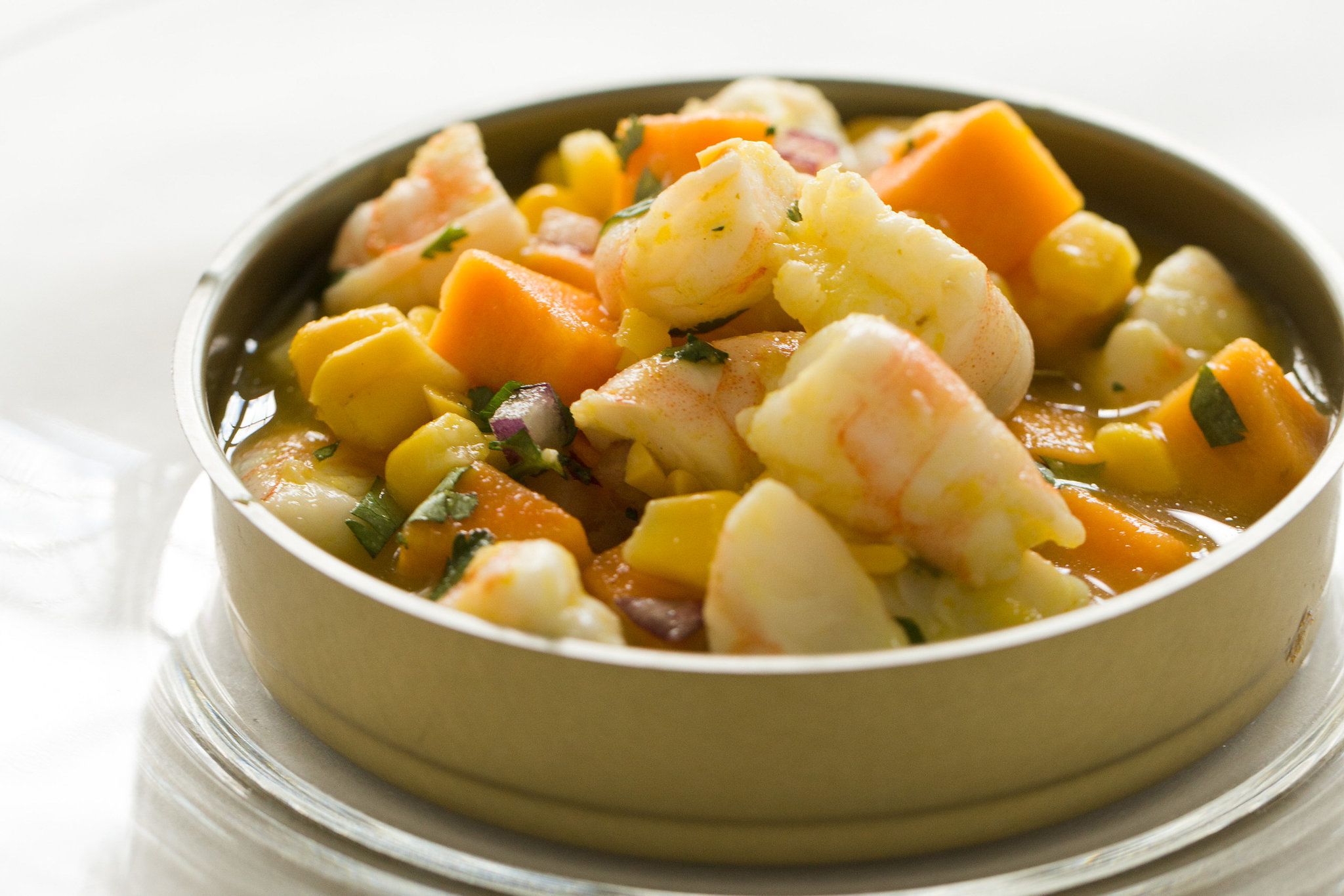A bowl of seafood stew with shrimp, potatoes, and carrots.
