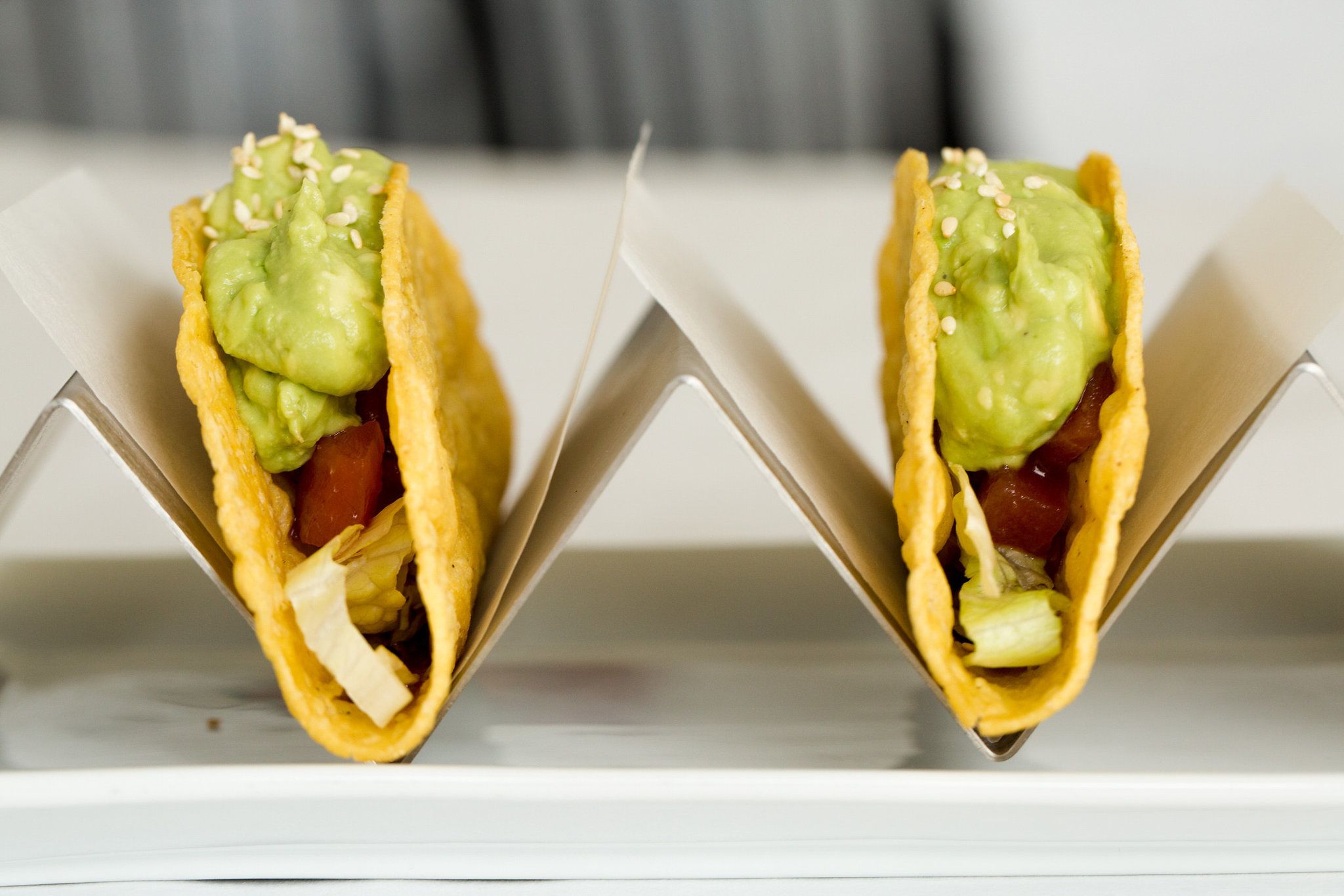 Two tacos with guacamole and sesame seeds on a white surface.