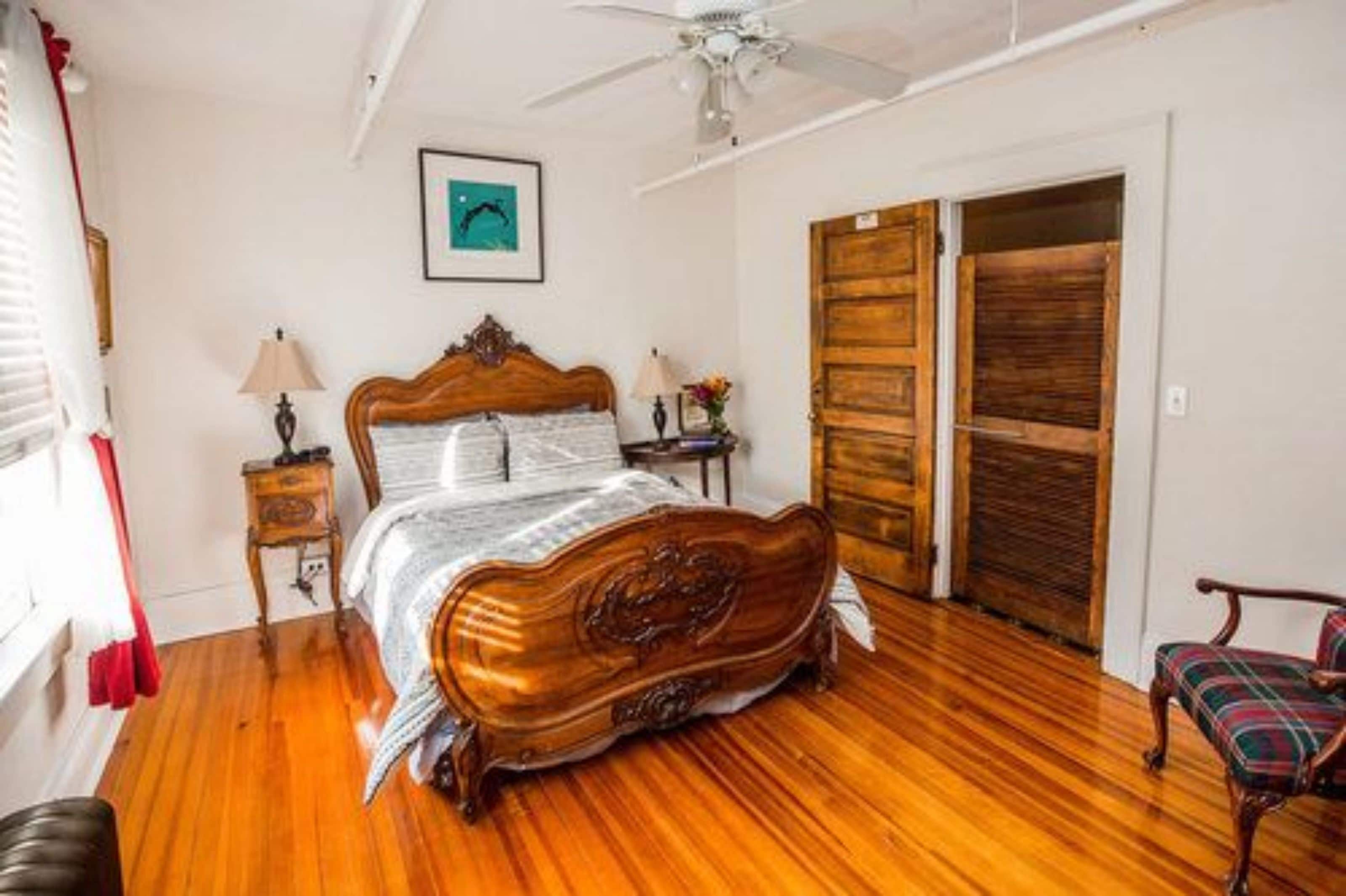 Une chambre avec un lit en bois, un ventilateur de plafond, une armoire en bois et une chaise.