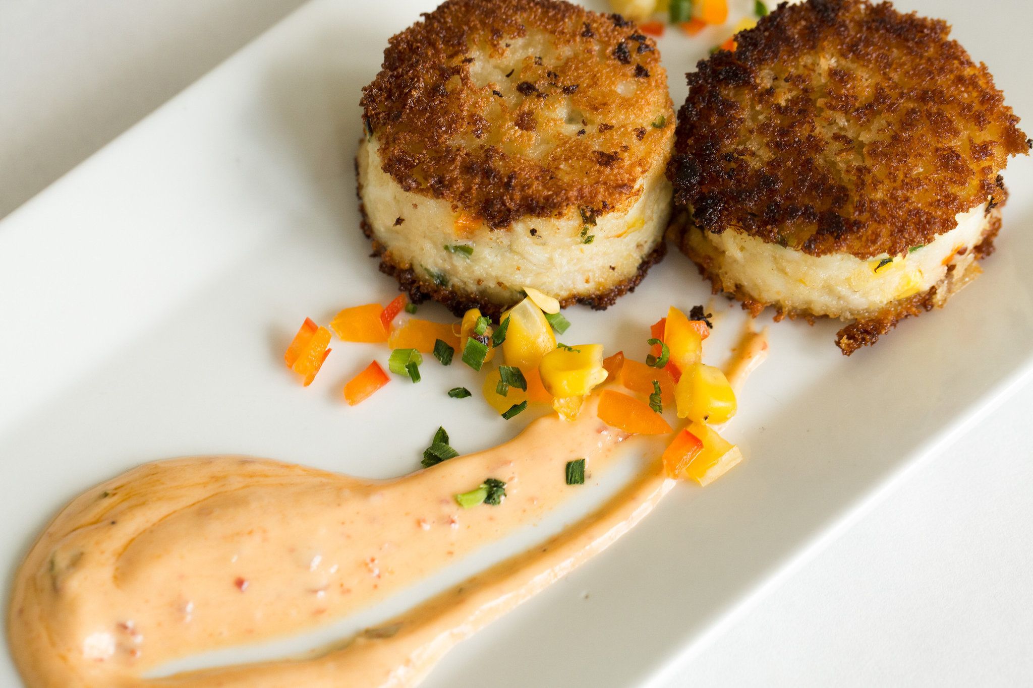 Two crab cakes with a creamy sauce and diced mango on a white plate.