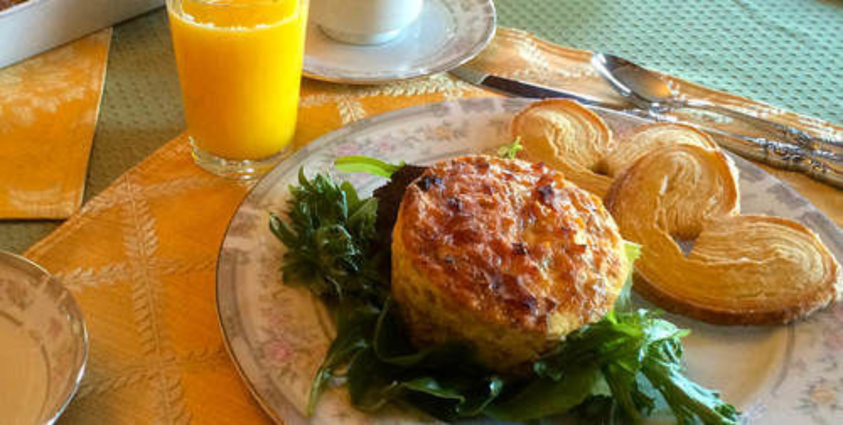 Une table mise pour le petit-déjeuner avec une assiette de nourriture, un verre de jus d’orange et un croissant.