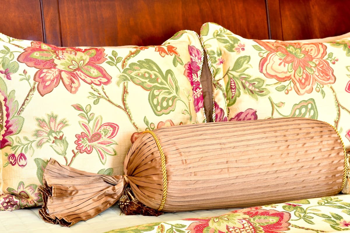 A bed with floral-patterned bedding and a rolled-up brown blanket.