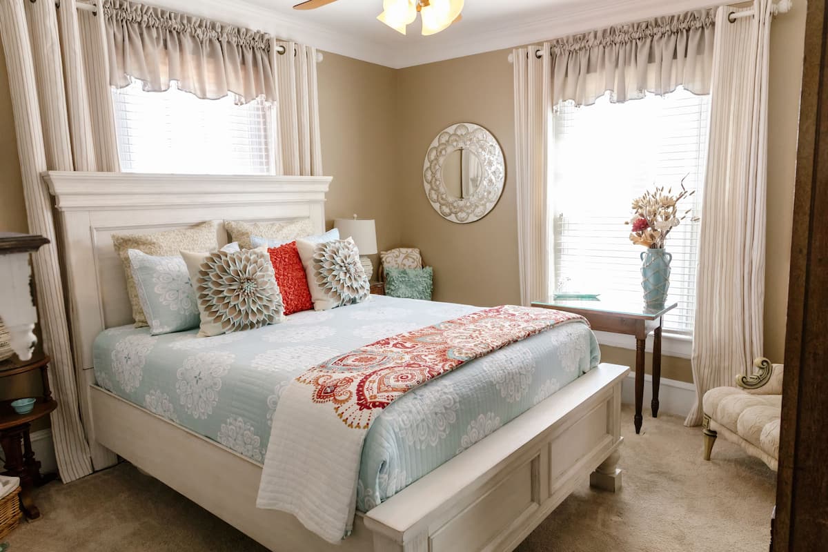 A bedroom with a large bed, a bedside table, a mirror, and a window with curtains.