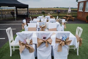 An outdoor wedding setup with tables and chairs, a tent, and a wooden fence in the background. - Tri-star Hotel (Birmingham)