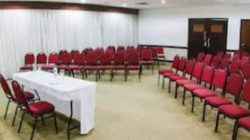 A conference room with rows of red chairs, a white table, and a projector screen.