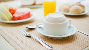 Ein Frühstückstisch mit einer Kaffeetasse, einem Glas Orangensaft und Tellern mit Speisen, darunter Wassermelone und Brötchen.