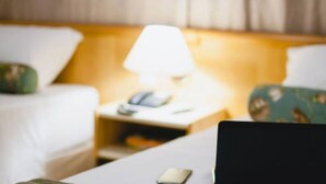 Ein Hotelzimmer mit einem Bett, einem Nachttisch mit Lampe und einem Laptop auf dem Tisch.