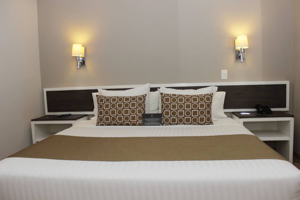 A hotel room with a large bed, two bedside tables, a nightstand, and two wall-mounted lamps.