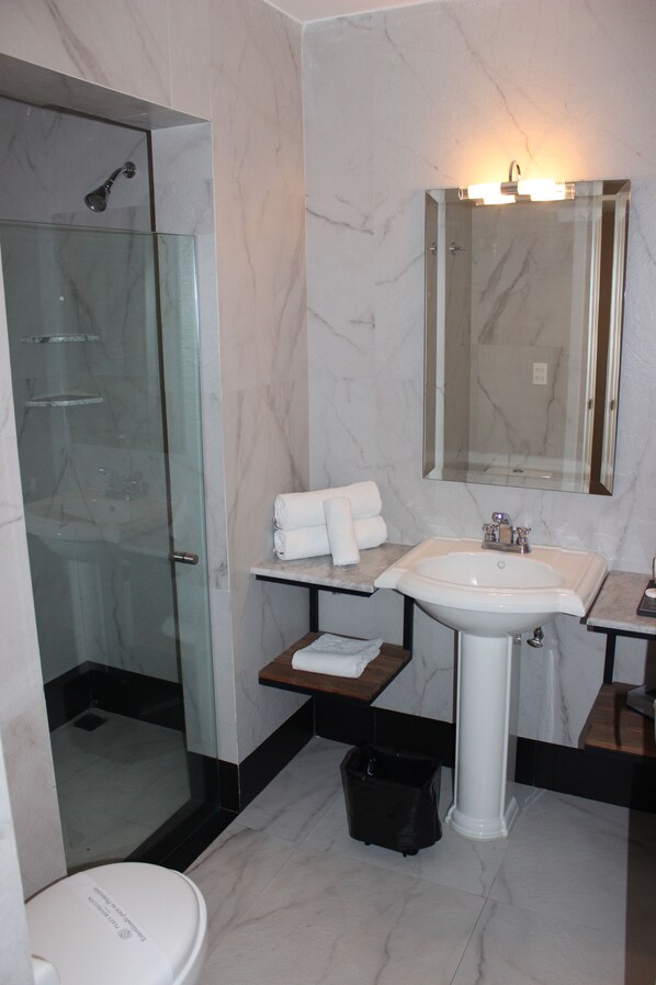 A bathroom with a glass-enclosed shower, a white sink, a mirror, and a small shelf with towels.